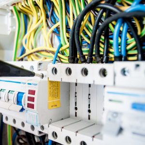 Hand of electrician working on a circuit breaker panel with colorful wires, ensuring safe electrical connections.